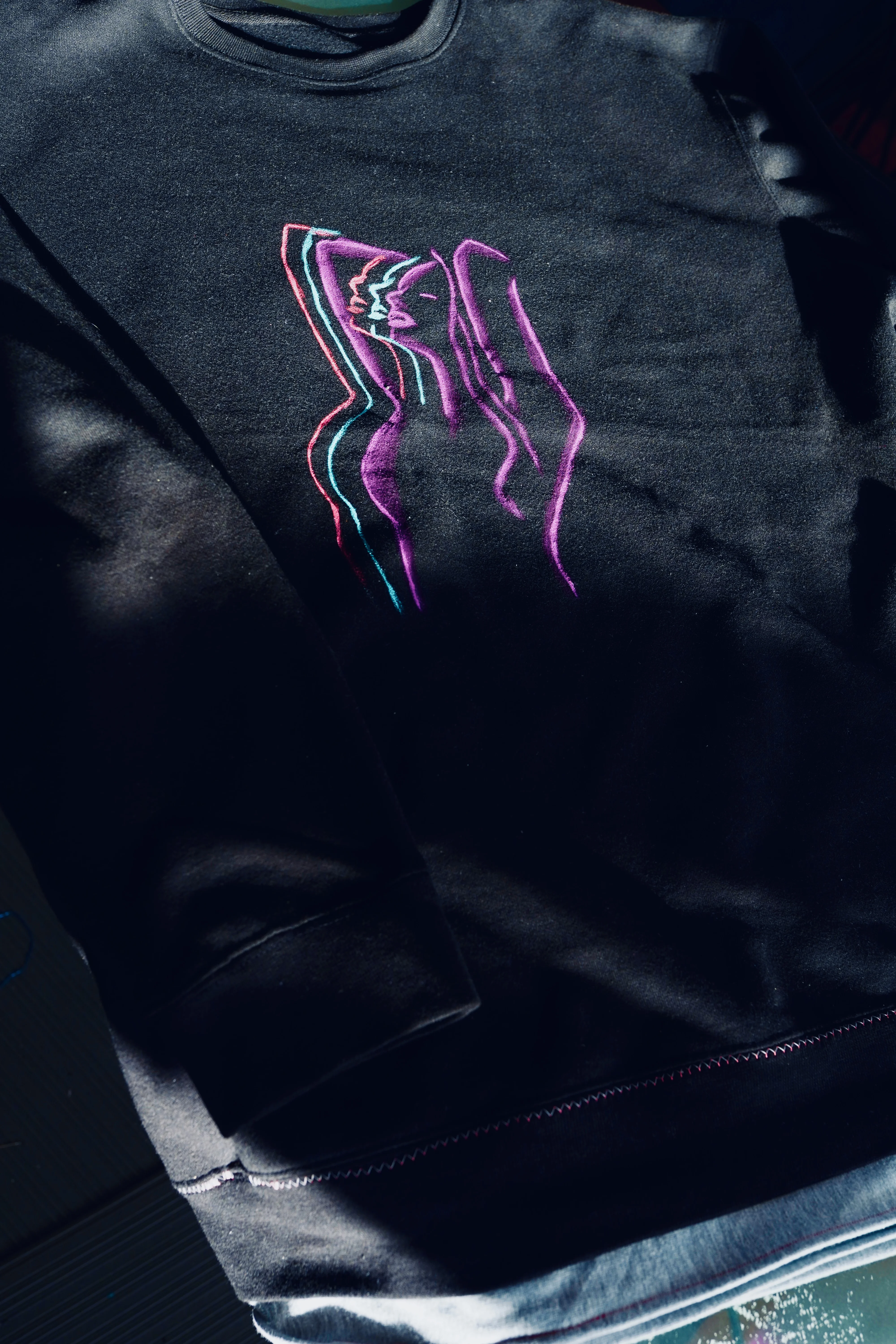 Black crewneck sweatshirt with minimalist embroidered neon linear kissing figures