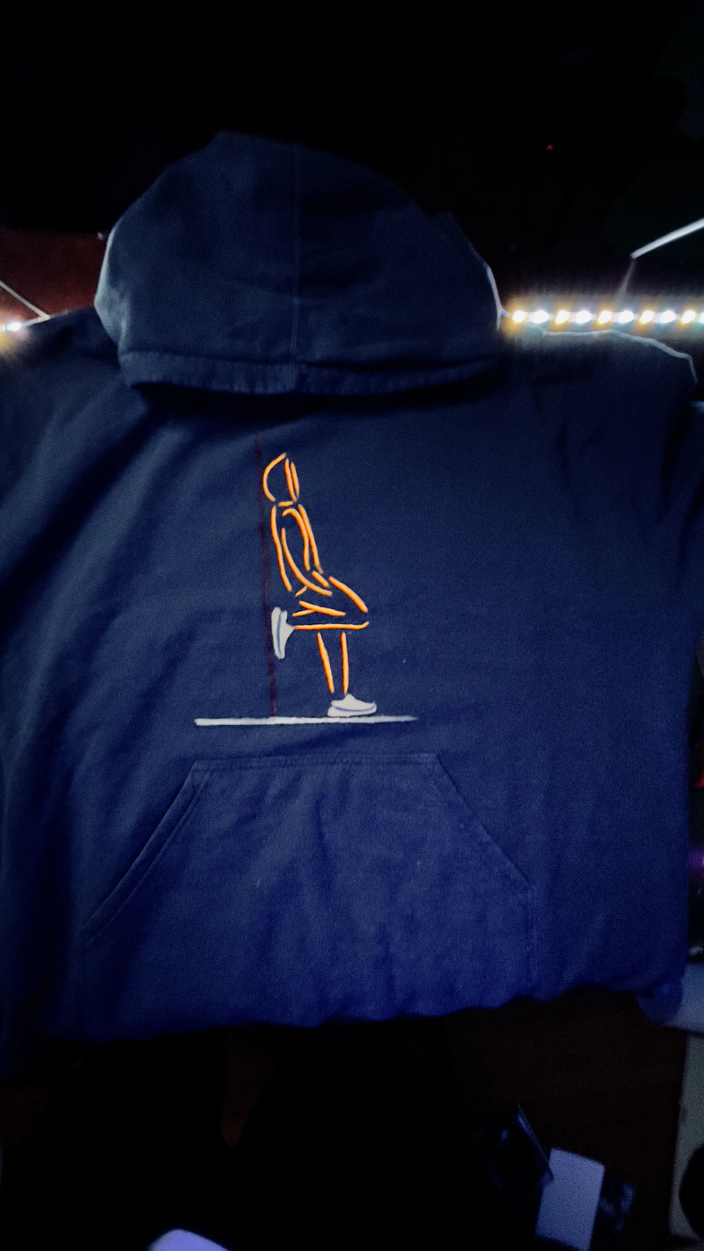 Model wearing black hoodie featuring minimalist embroidered orange figure